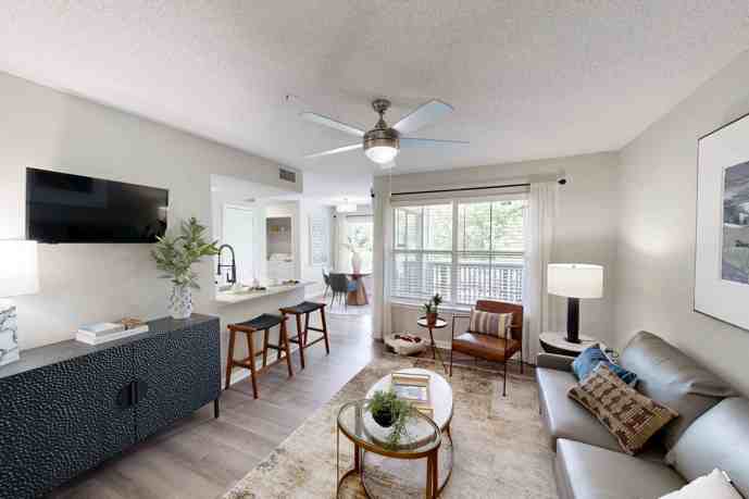 Furnished apartment living and TV area with the small kitchen and dining area in the background